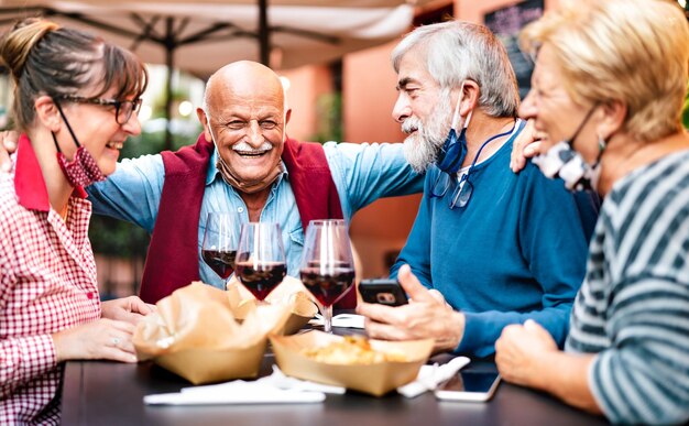 Amigos adultos bebendo vinho no bar do restaurante usando máscaras abertas