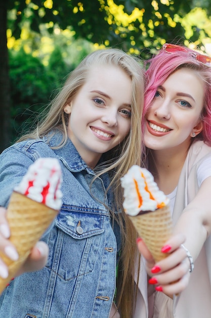 Amigos adultos jóvenes hipster abrazándose mientras pasan el rato en la ciudad. Dos mujeres jóvenes riendo y caminando disfrutando de un estilo de vida de vacaciones sin preocupaciones. Dos amigas bonitas comiendo helado en la ciudad