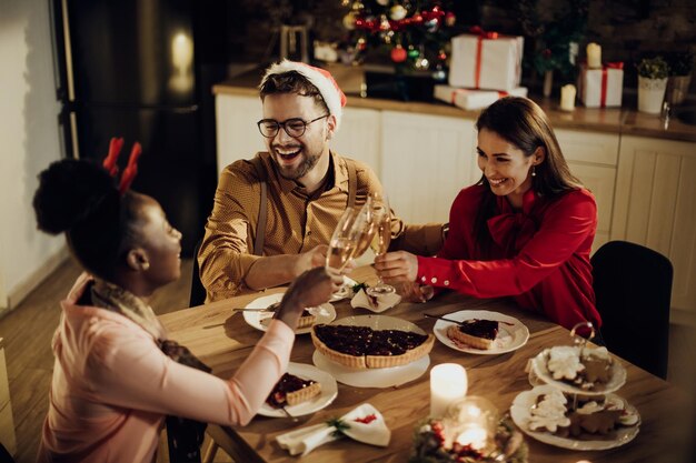 Amigos alegres brindando com champanhe ao jantar de Natal em casa