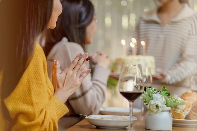 Amigos alegres curtindo a festa de aniversário em casa Irmã asiática torcendo bebendo vinho tinto comemorando com bolo de aniversário