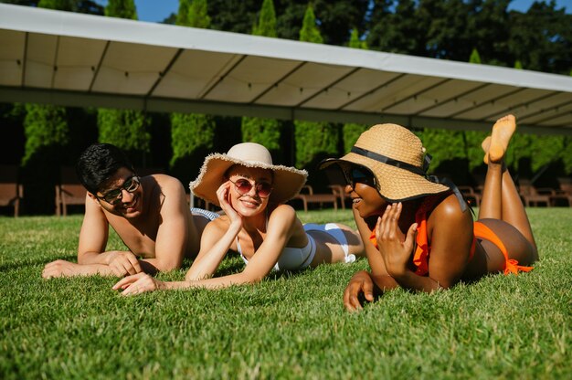 Amigos alegres descansam na grama perto da piscina