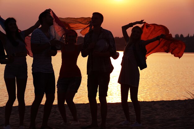 Amigos alegres divirtiéndose en la orilla al atardecer al aire libre