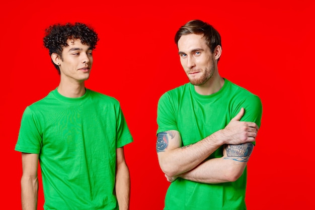 Amigos alegres em camisetas verdes estão ao lado do fundo vermelho