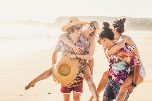 Amigos alegres, un par de personas, niñas y niños se divierten juntos en el berach en las vacaciones de verano juntos: los hombres llevan a las mujeres y todos sonríen y ríen mucho