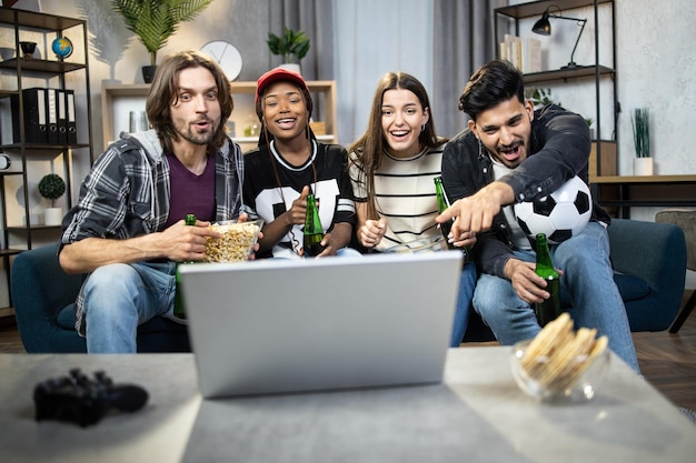 Amigos alegres que usan una computadora portátil para ver un partido de fútbol