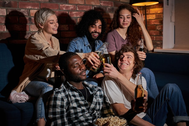 Amigos alegres sentados en casa y viendo el partido de fútbol en la televisión. Su equipo favorito está ganando, concepto de victoria. Animando, bebiendo cerveza, descansando