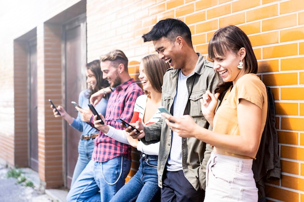 Amigos alegres usando telefone celular enquanto estão de pé junto à parede ao ar livre