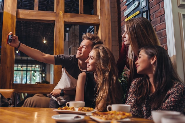 Foto amigos animados tirando selfie com smartphone sentado à mesa saindo à noite