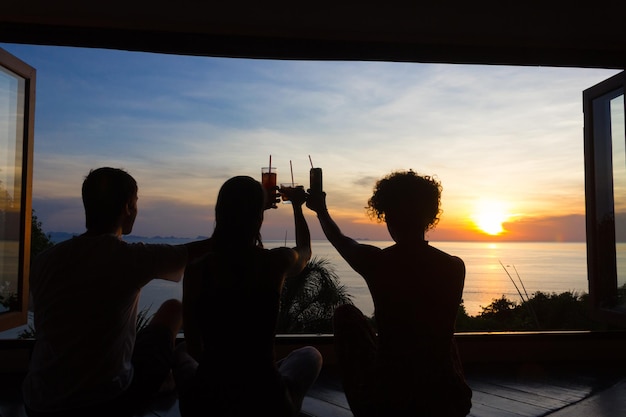 Amigos animando al atardecer en el resort en Koh Phangan, Tailandia, los jóvenes se levantan sus copas