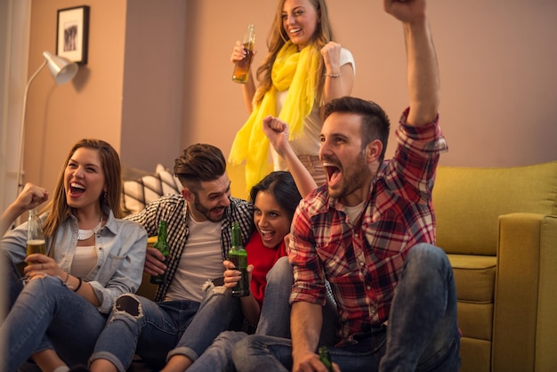 Amigos animando mientras ven un partido de fútbol en casa