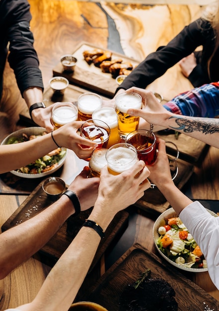 Foto amigos animando vasos de cerveza en una mesa de madera cubierta con comida deliciosa vista superior de personas cenando en el bar restaurante concepto de estilo de vida de alimentos y bebidas