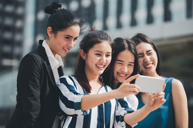 Amigos asiáticos de la empresaria de la forma de vida que sonríen y que se divierten caminando el selfie en la ciudad