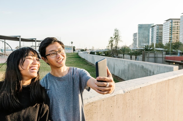 Amigos asiáticos felices divirtiéndose mientras toman selfie con smartphone al aire libre