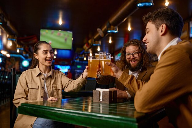 Amigos assistindo jogo de futebol tilintando descanso de caneca de cerveja no bar esportivo