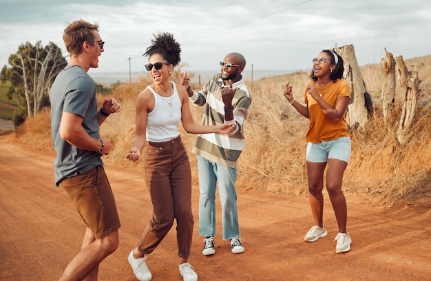 Los amigos bailan y la naturaleza con un grupo de hombres y mujeres que se divierten al aire libre durante un viaje o una aventura juntos Vacaciones de verano y libertad con jóvenes bailando en un camino de arena en el desierto