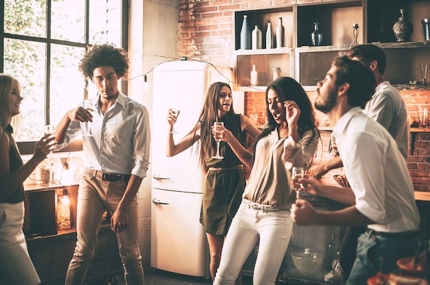 Amigos bailando. Jóvenes alegres bailando y bebiendo mientras disfrutan de la fiesta en casa en la cocina