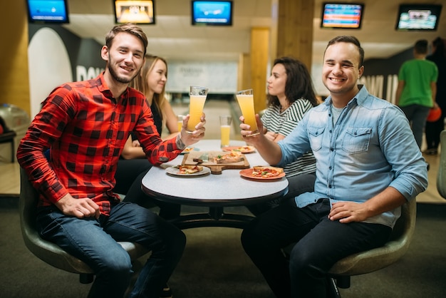 Amigos bebe y come pizza en el club de bolos