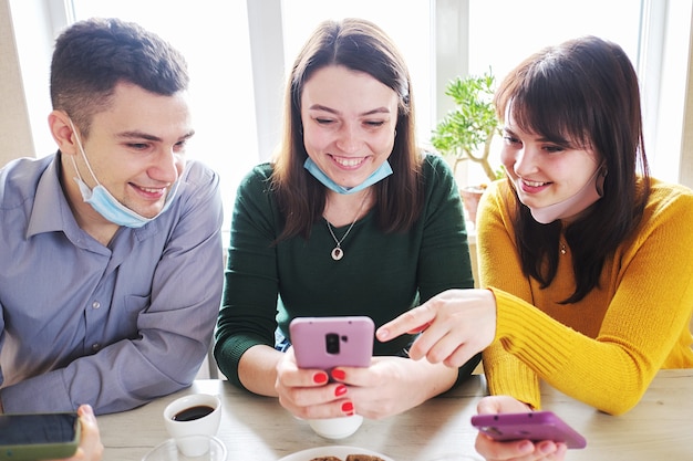 Amigos beben café en una cafetería y se divierten con los teléfonos móviles