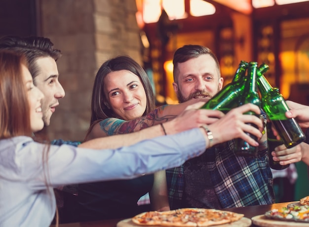 Amigos, bebendo e comendo pizzas em um bar