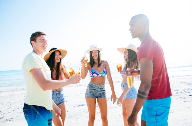 Foto amigos con bebidas mientras están de pie en la playa contra el cielo