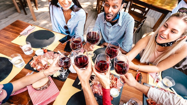 Amigos bebiendo vino tinto en el bar del restaurante con mascarilla abierta
