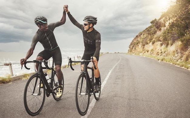 Amigos en bicicleta y hombres chocando cinco en la carretera divirtiéndose juntos en bicicleta al aire libre Diversidad de éxito y trabajo en equipo de ciclistas masculinos en bicicleta montando en la calle haciendo ejercicio o entrenando en asfalto