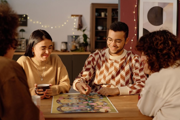 Amigos biraciales sentados en la mesa mirando a un hombre que agita los dados antes de lanzarlos