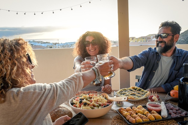 Amigos brindando copas de cerveza en la mesa en la terraza durante la puesta de sol
