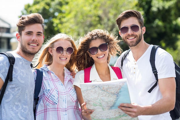 Amigos de cadera sosteniendo el mapa y mirando a la cámara al aire libre