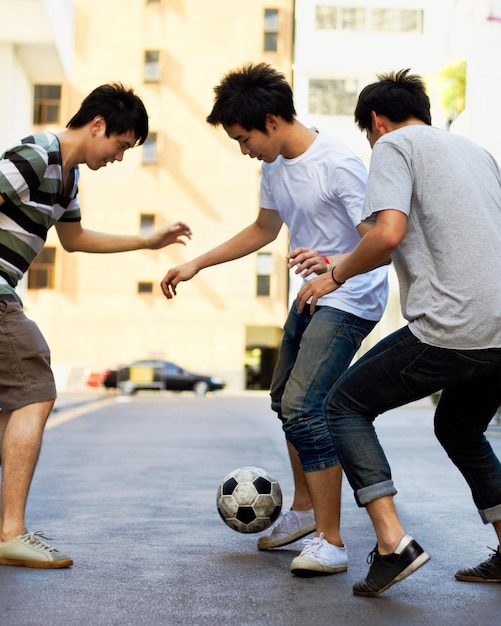 Foto amigos en la calle jugando al fútbol juntos por diversión deportiva y energía feliz con juegos urbanos en corea juegos para niños amistad y grupo de adolescentes en la carretera con un fin de semana de pelota de fútbol en una ciudad asiática