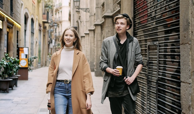 Amigos caminando juntos por una calle estrecha. Asimiento de la muchacha en la cámara de las manos. Disfrutan del paseo conjunto.