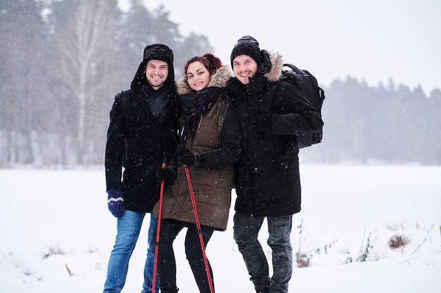 Amigos caminhando na floresta nevada fria ficam em um abraço e olham para a câmera.