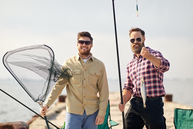 Amigos con caña de pescar peces y aparejos en el muelle