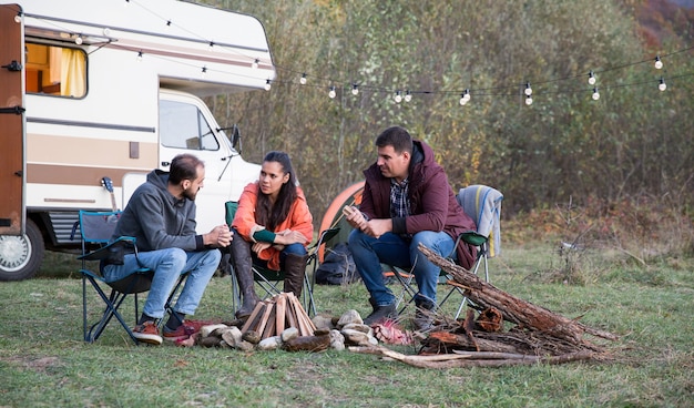 Amigos caucasianos acampando juntos nas montanhas com sua van de campista retrô. Preparando uma fogueira.