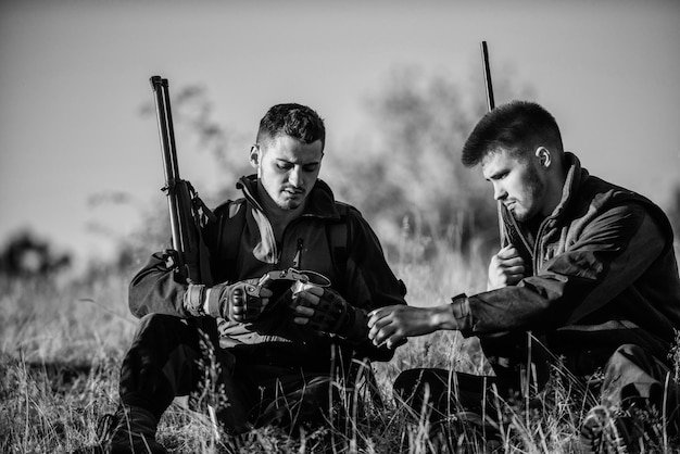 Los amigos de los cazadores disfrutan del ocio Cazando con amigos, pasatiempos, ocio Cazadores satisfechos con la bebida de captura, bebida caliente Descanso para el concepto de hombres reales Cazadores con rifles relajándose en el entorno natural