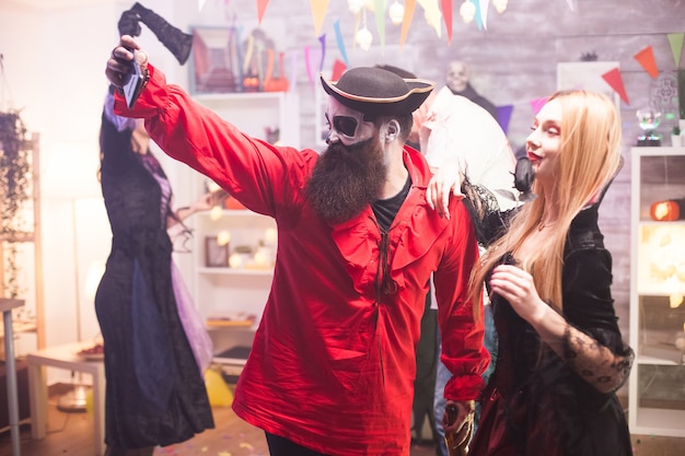 Amigos cercanos con disfraces de piratas y vampiros tomando un selfie en la celebración de Halloween.