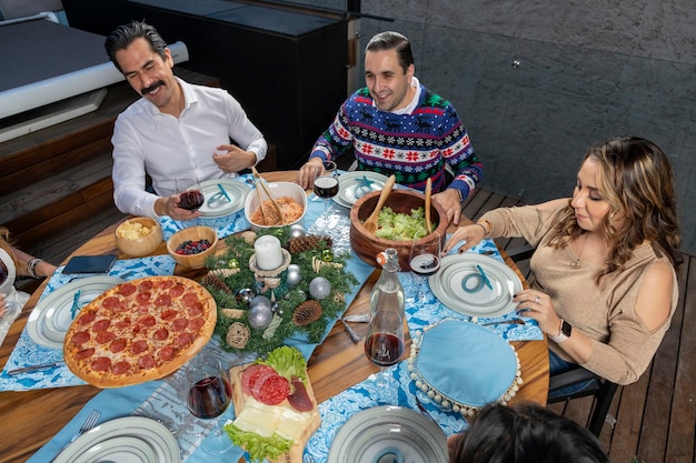 Amigos charlando alegremente sentados en una mesa con decoración azul en la cena de Navidad