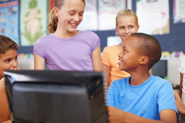 Amigos en clase de computación Un grupo de lindos escolares sentados y parados alrededor de una computadora durante la clase