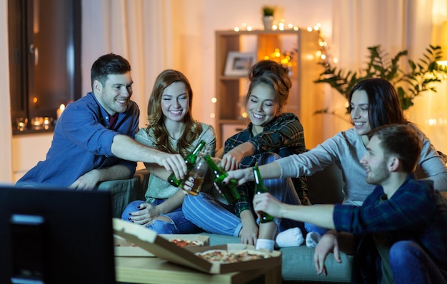Amigos com bebidas e pizza a ver televisão em casa.