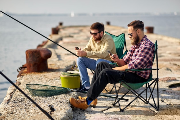 Amigos com smartphones a pescar no cais no mar.