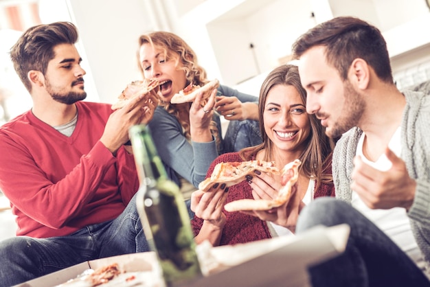 Foto amigos comendo pizza. eles estão fazendo festa em casa, comendo pizza e se divertindo.