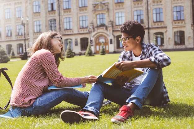 Amigos conversam juntos no campus. Estudante afro-americano de sorriso nos vidros com livros e uma menina perto da faculdade.