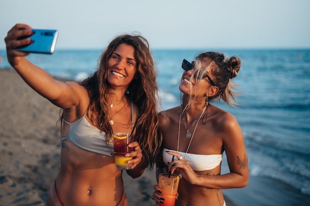 Amigos curtindo férias juntos e tirando selfie na praia usando smartphone