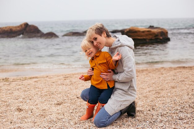 Amigos da família felizes para sempre conceito Mãe sorridente e filho brincando juntos perto do mar no outono