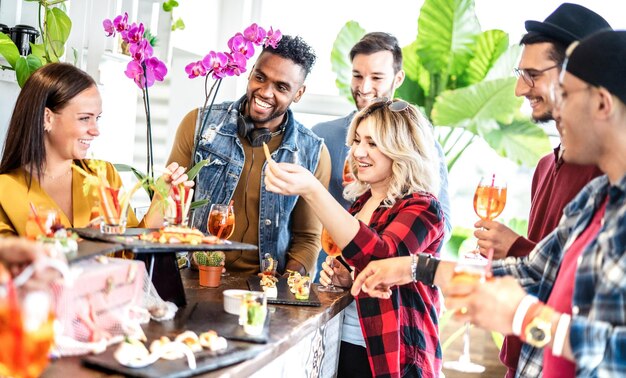 Amigos da moda multirraciais se divertindo no jantar chique no buffet de aperitivos bebendo coquetéis