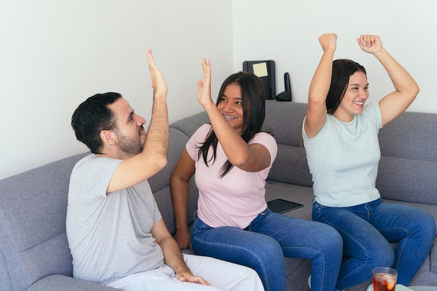 Amigos dando highfive enquanto comemoram o gol da vitória Os fãs de futebol estão desfrutando de bebidas e lanches enquanto estão sentados no sofá Eles estão se divertindo em casa