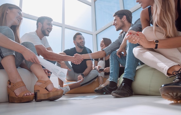 Foto amigos dándose la mano, sentados en el suelo de la nueva oficina. el concepto de una startup