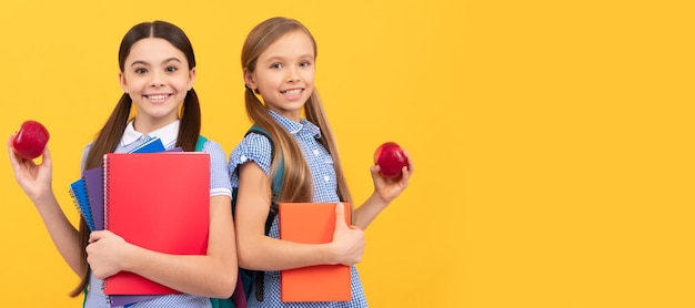 Amigos das meninas da escola Alunos felizes com livros seguram maçãs orgânicas vitamínicas escola de fundo amarelo