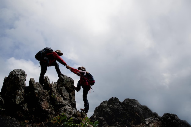 Amigos de caminhada de pessoa ajudando uns aos outros em uma montanha Homem e mulher dando uma mão amiga e estilo de vida ativo e adequado Casal da Ásia caminhadas se ajudam conceito de trabalho em equipe de amizade