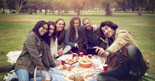 Amigos de comida divertidos e agora para capturá-lo foto de jovens amigos fazendo um piquenique lá fora